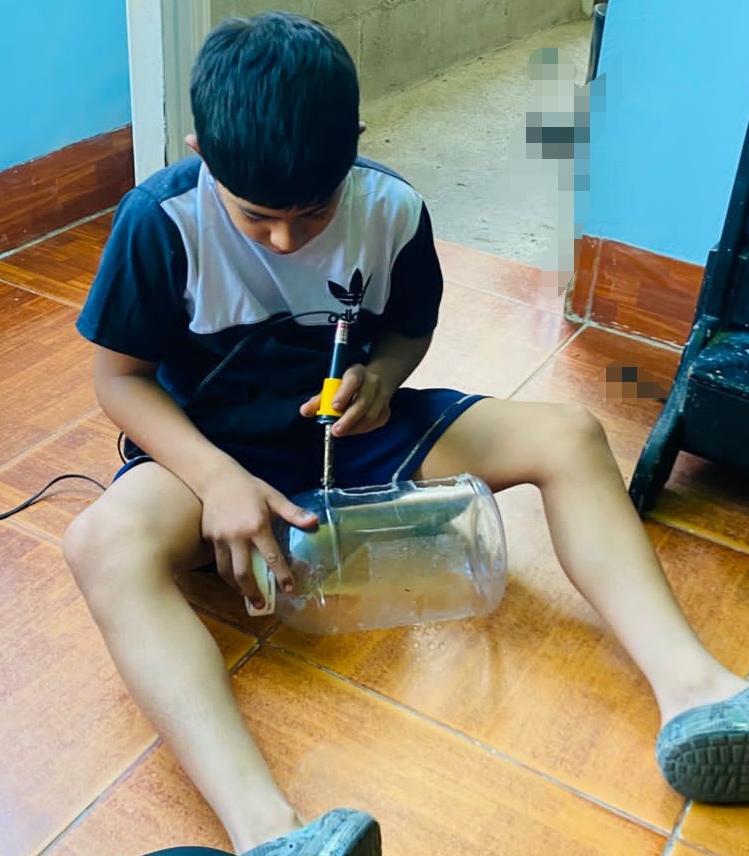 Estudiante adaptando un recipiente plástico con herramienta térmica para siembra